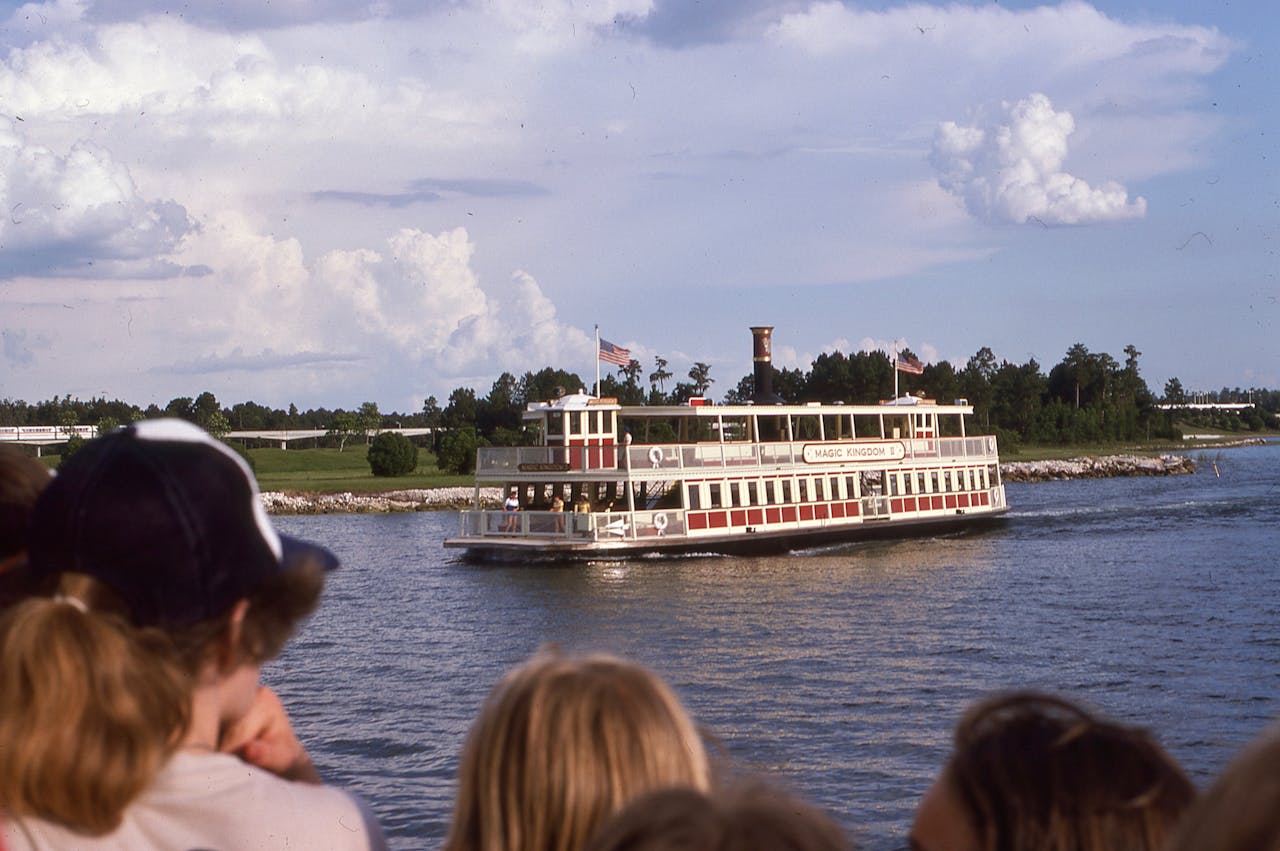 Tourboat cruises on a lake at Magic Kingdom, Orlando, with tourists in the foreground.