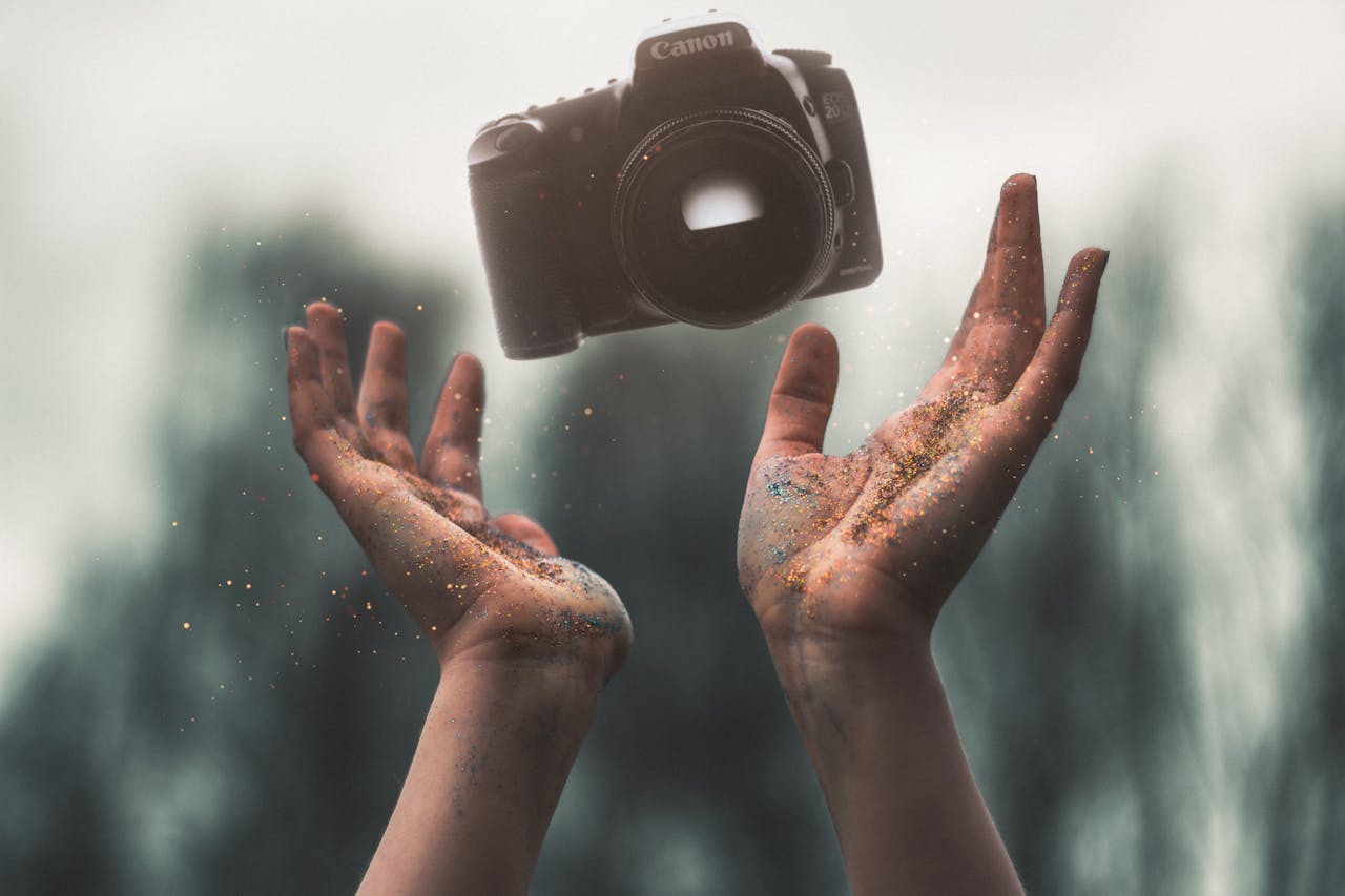 Hands tossing a DSLR camera with a magical sparkle effect in nature.